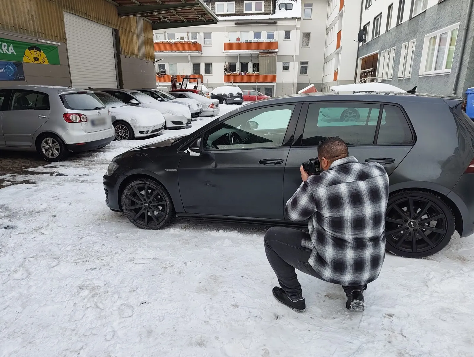 Herr Khalek dokumentiert den Schaden an einem schwarzen VW Golf im Schnee